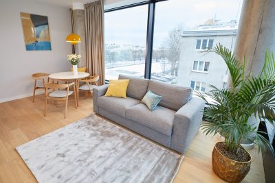 Sofa z żółtą poduszką, palma i stół jadalny przy oknach